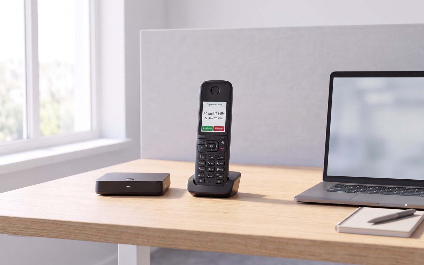 DECT handset on its base station showing the caller name «PC und IT Hilfe» on an incoming call, next to a laptop on the desk